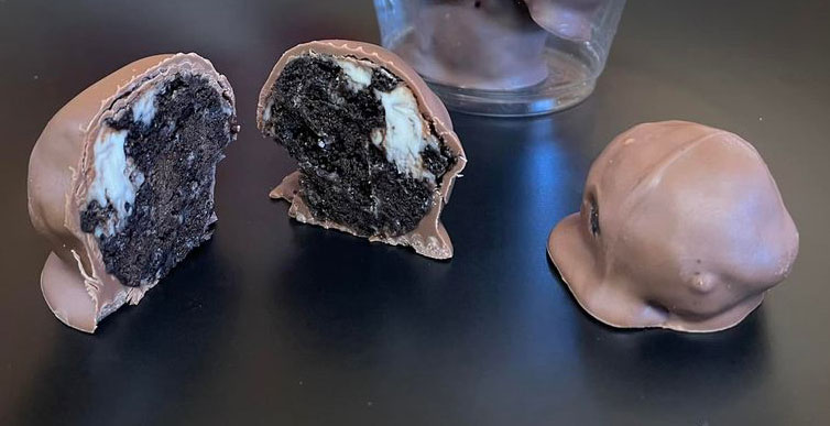 photo of two original oreo balls, one cut in half showing a mix of crushed oreo cookies and coconut covered with chocolate