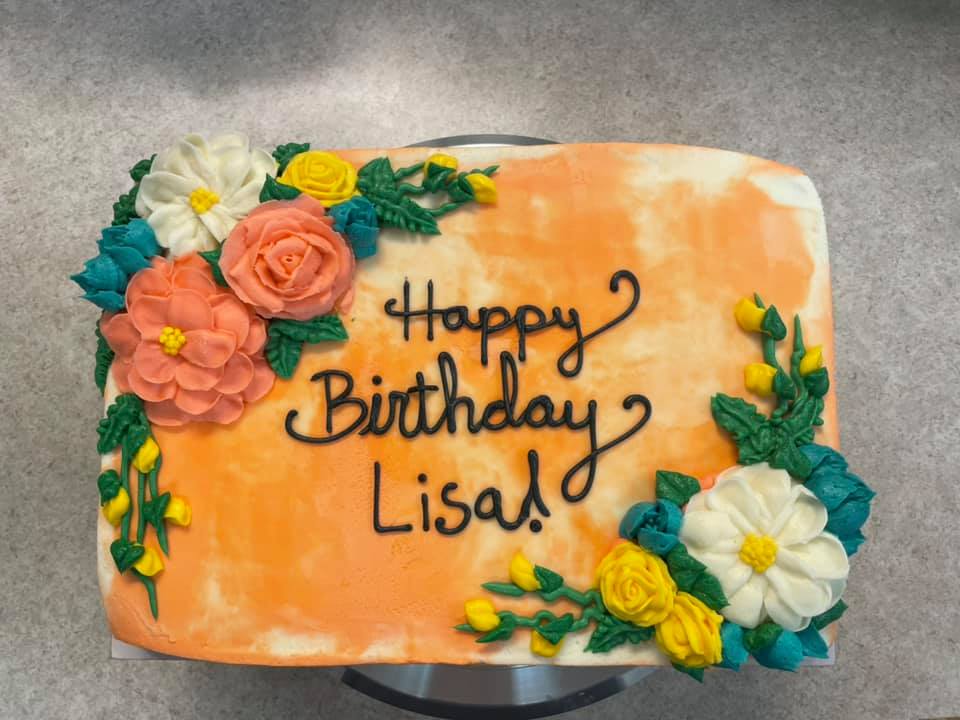 picture of a 1/4 sheet cake decorated with flowers and leaves on opposite corners with a decorative happy birthday Lisa in the center