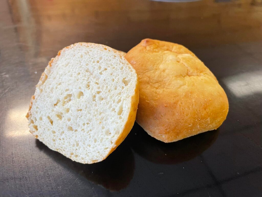 picture of gluten-free hamburger bun cut in half with the bottom half open and leaning on the top half