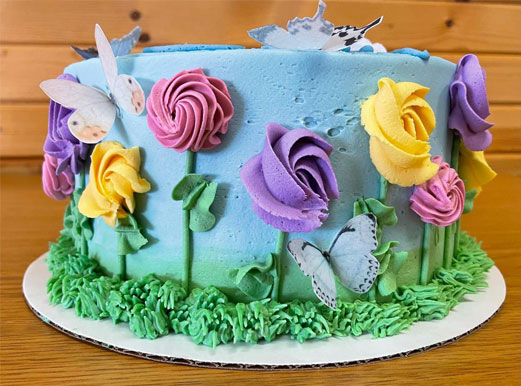 picture of a gluten-free layer cake with blue frosting and 3 D frosting flowers growing up the sides with butterfly accents