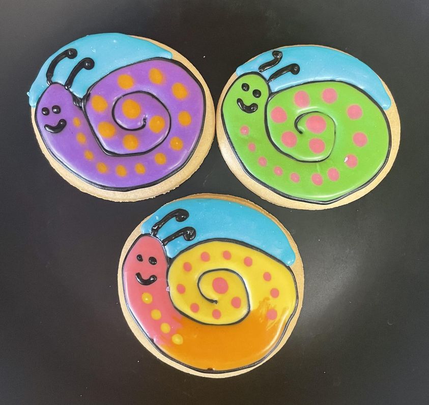 Three round cutout sugar cookies with colorful snails frosted on top
